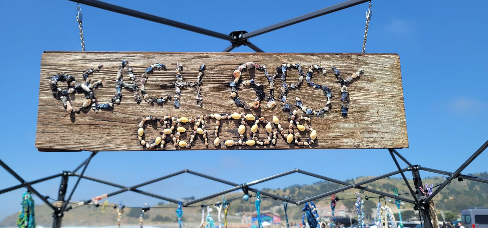 Beach Gypsy Creations wooden sign, letters made of shells, hanging from the beach tent