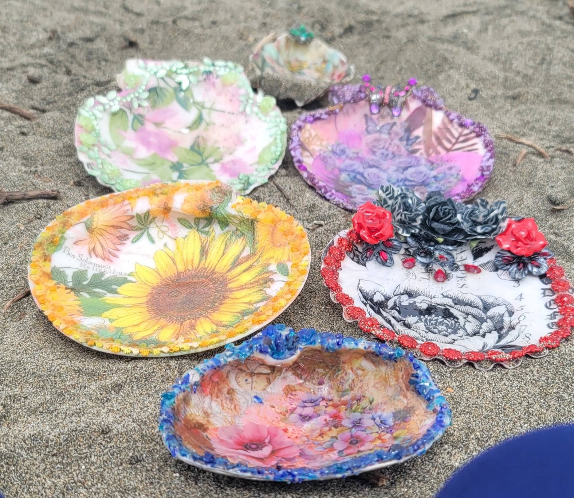 Five painted shells on sand: sunflower, peony, bloom bowl, green and purple scallops